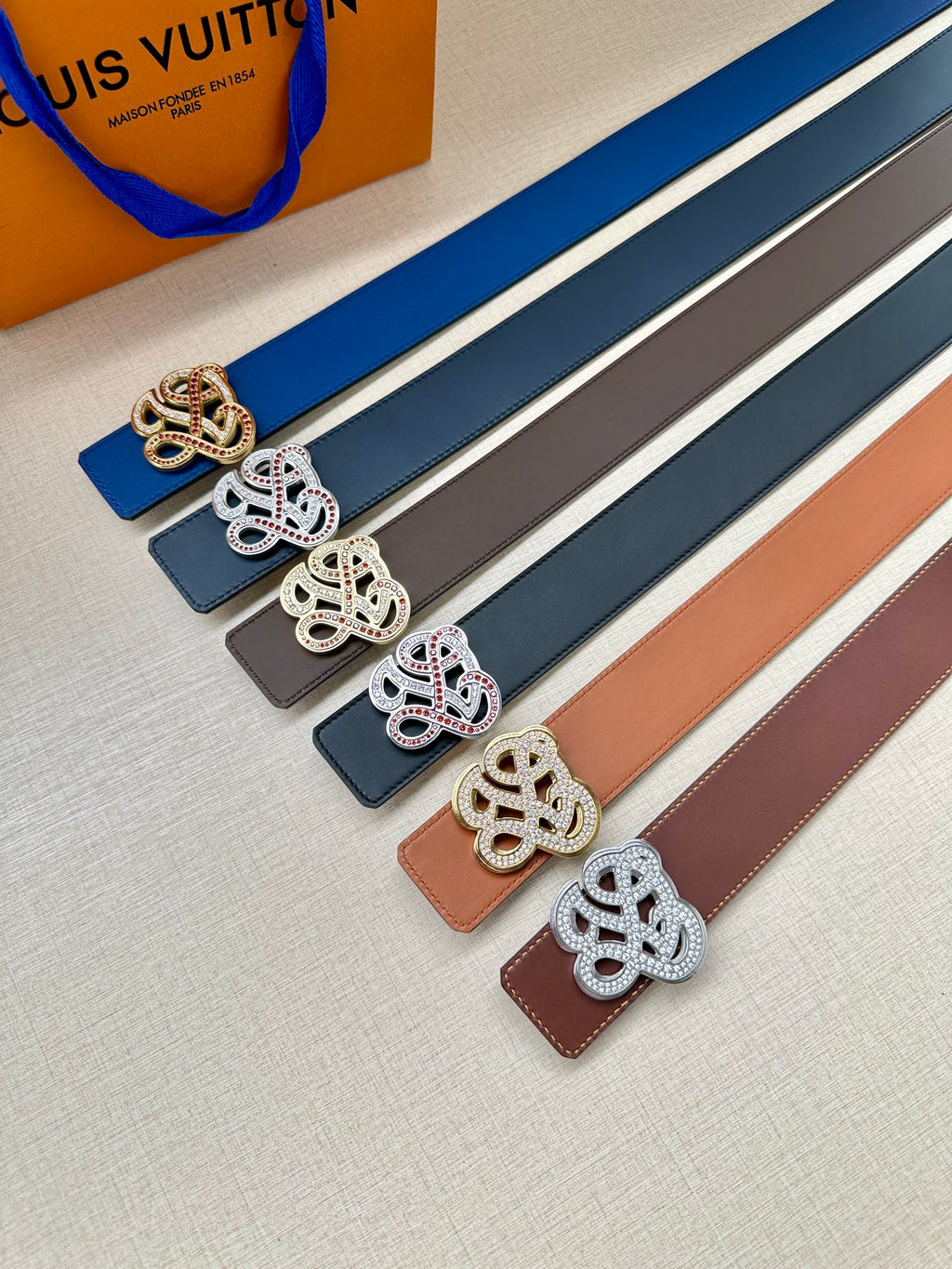 Assorted leather belts with logo buckles in gold, silver, and dark colors
