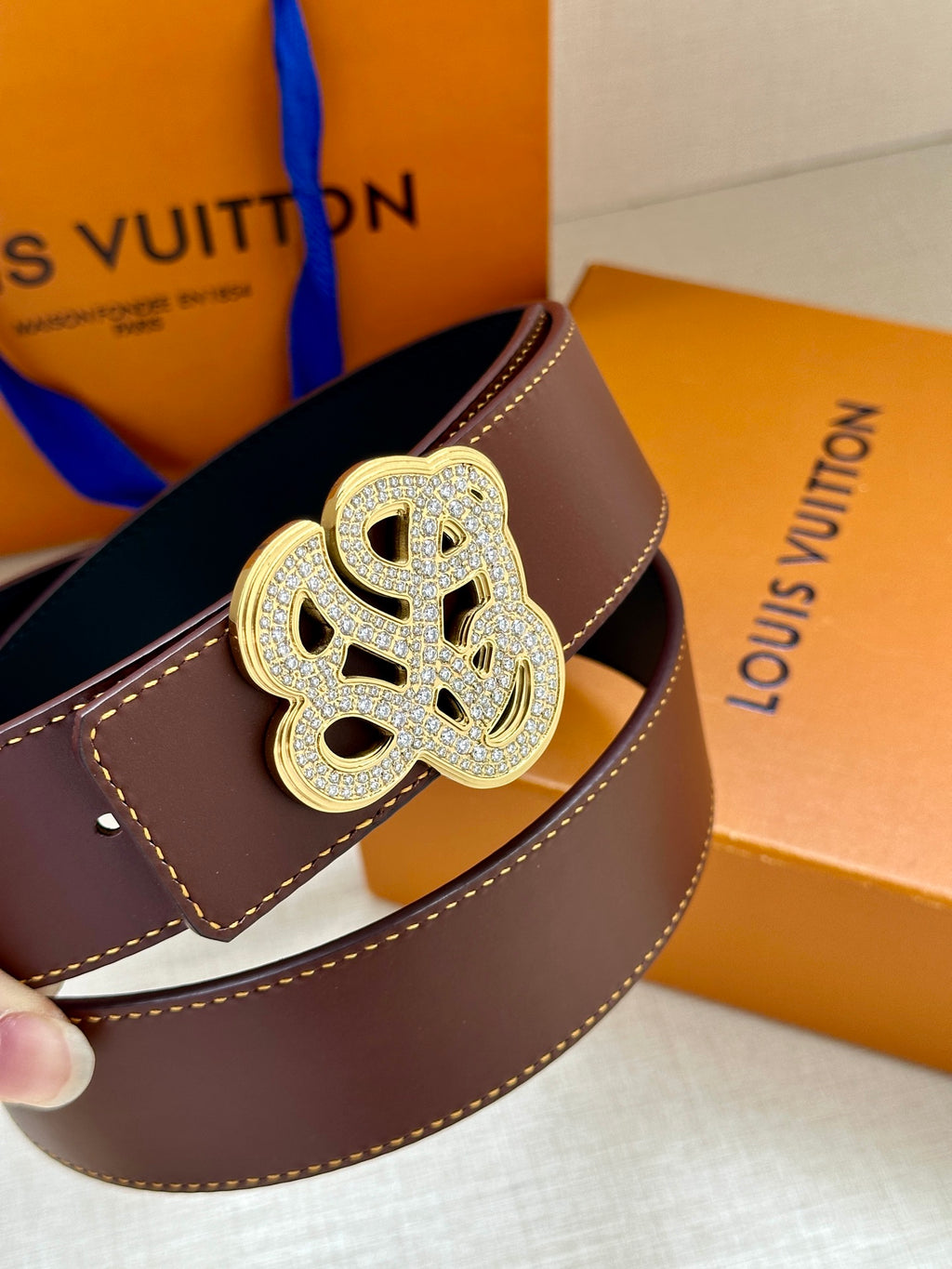 Brown leather belt with gold-tone logo buckle, close-up angle