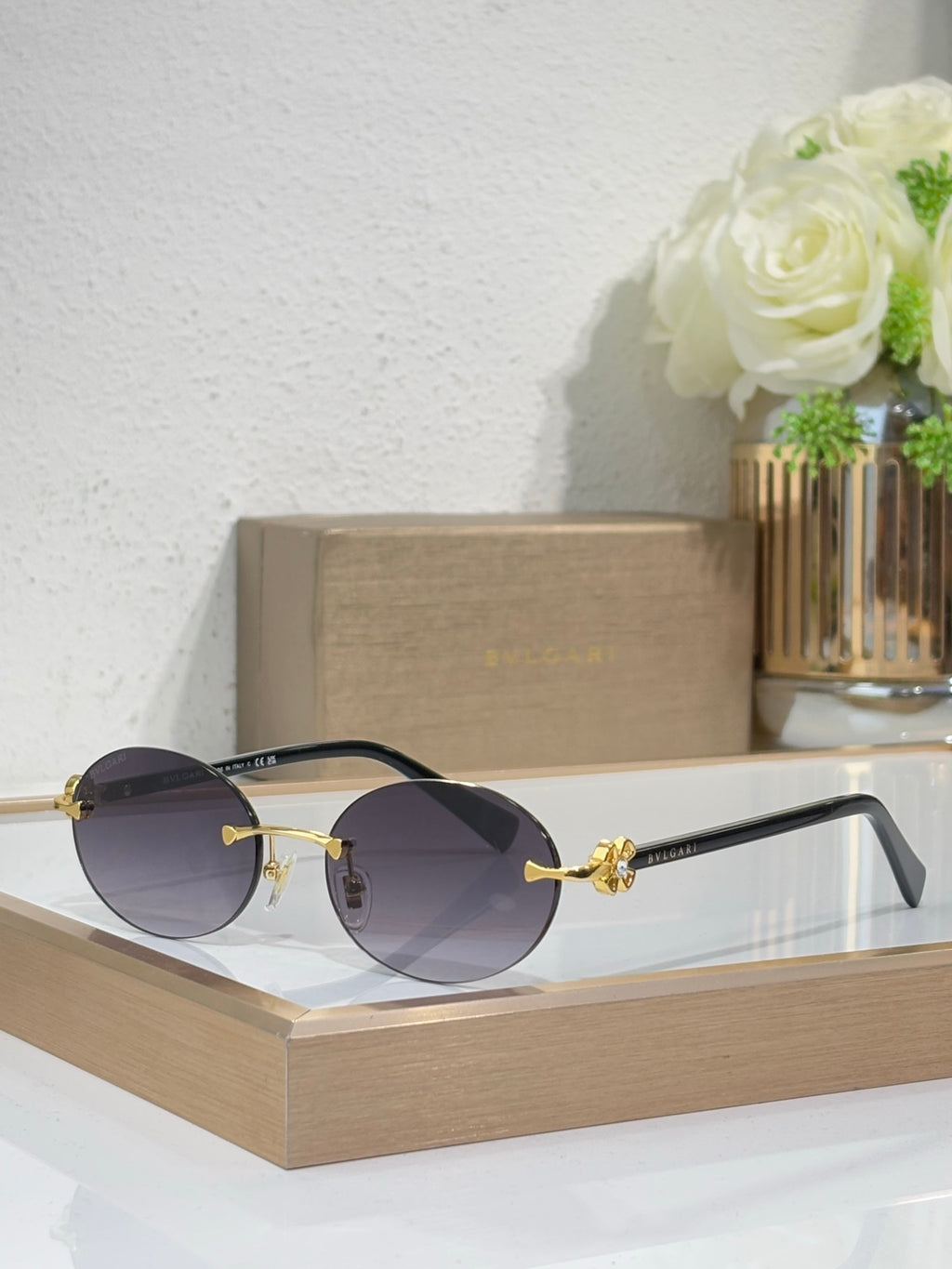 Gold-tone sunglasses with dark gray lenses and black temples, round lenses, jewel detail.