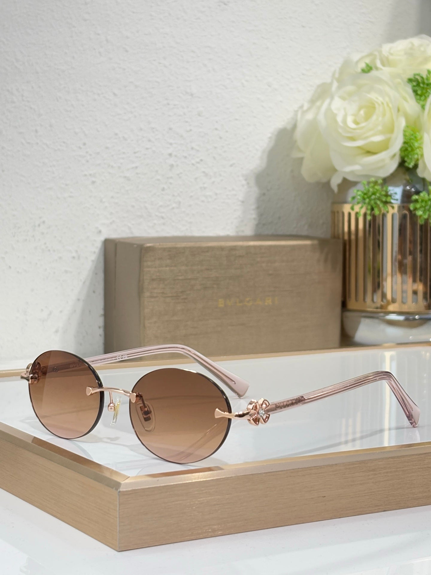 Rose gold sunglasses with light brown lenses and pink temples, round lenses, floral detail.