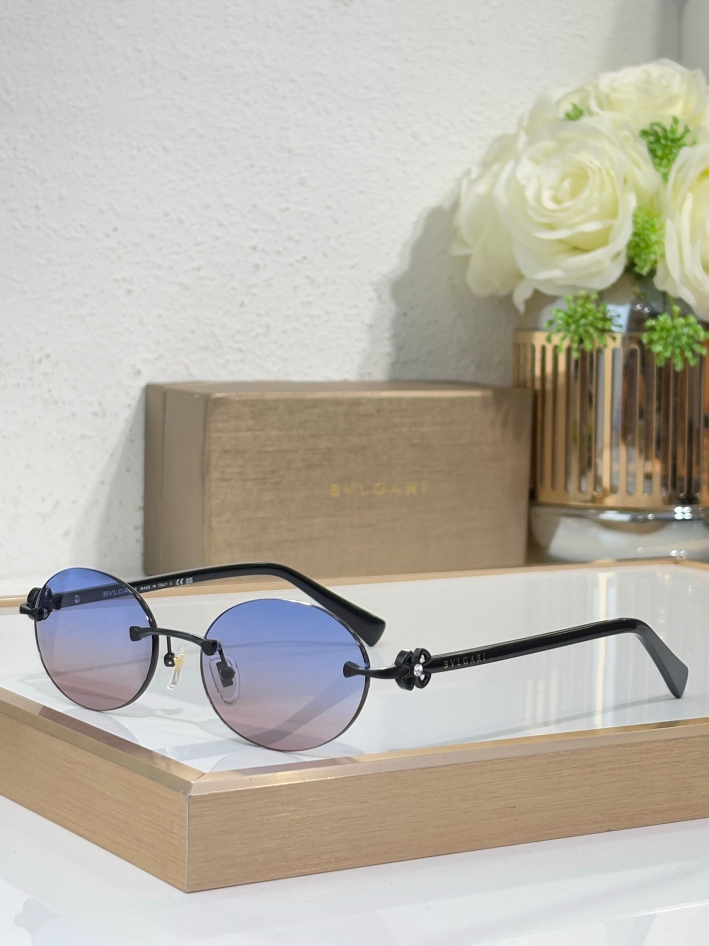 Blue-tone sunglasses with blue lenses and black temples, round lenses, small gold emblem.