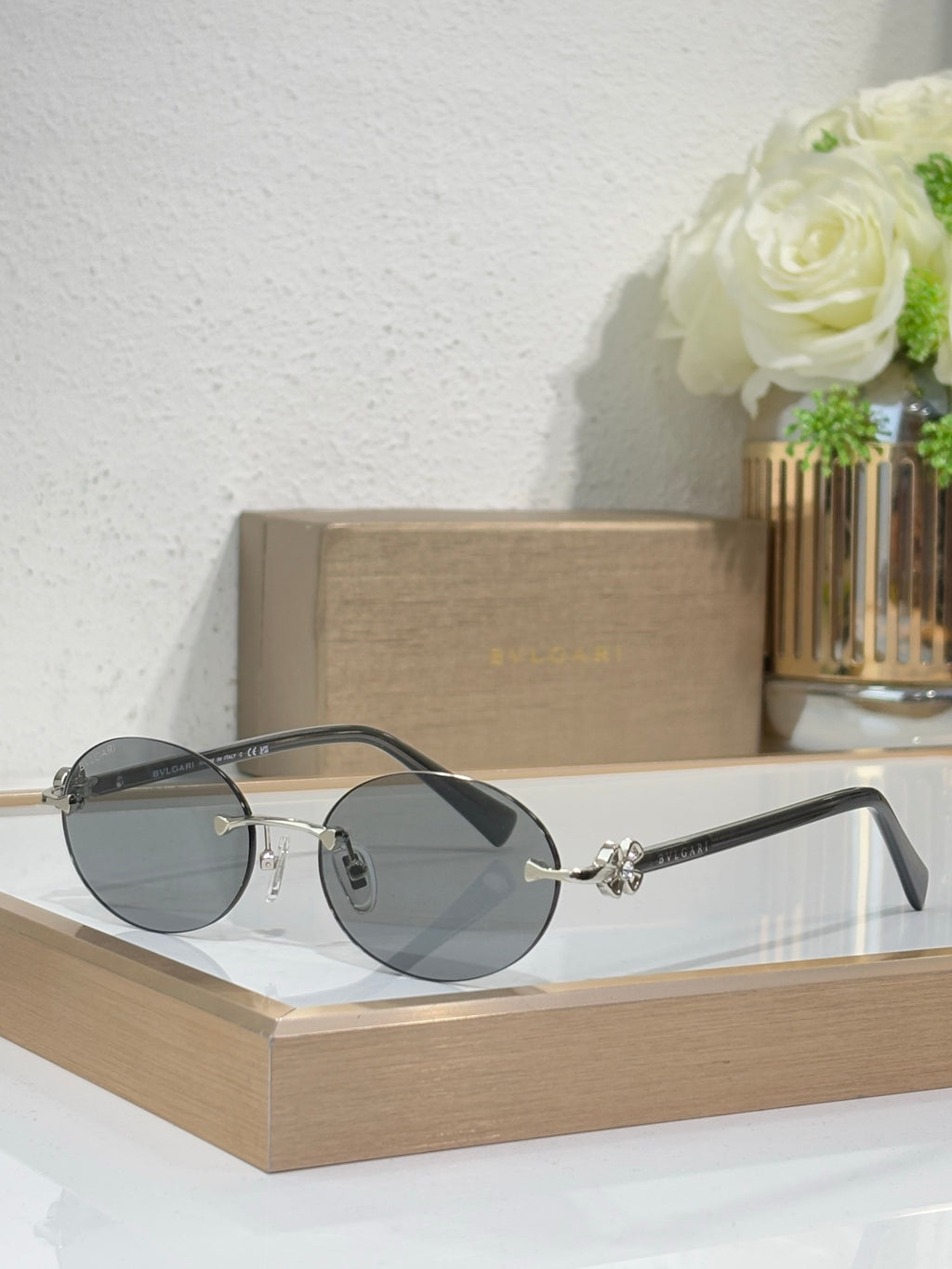 Silver-tone sunglasses with dark gray lenses and black temples, round lenses, small emblem.