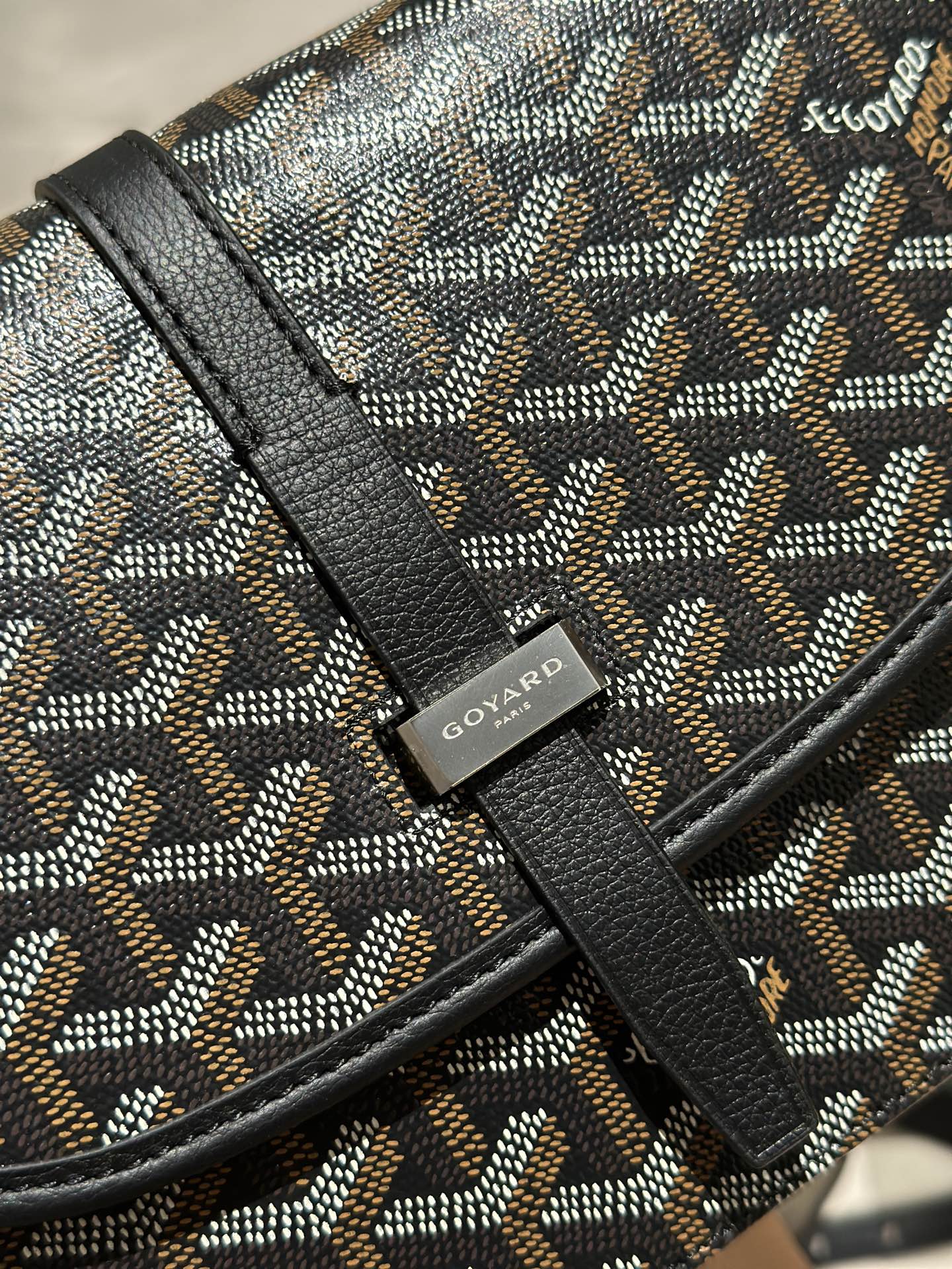 Goyard crossbody bag close-up of patterned canvas with black leather trim and logo patch