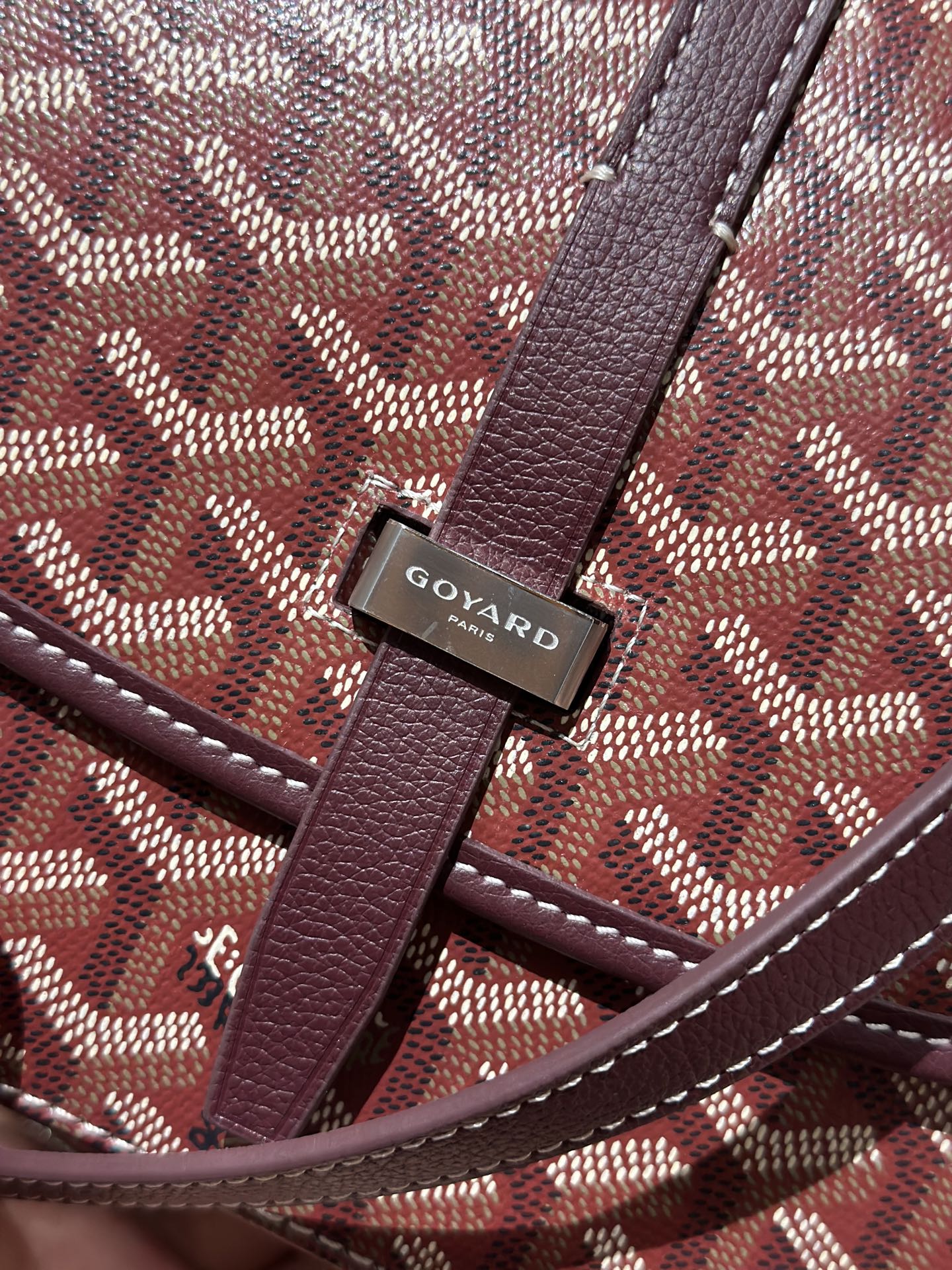 Goyard flap closure hardware with Goyard logo on maroon leather and patterned canvas