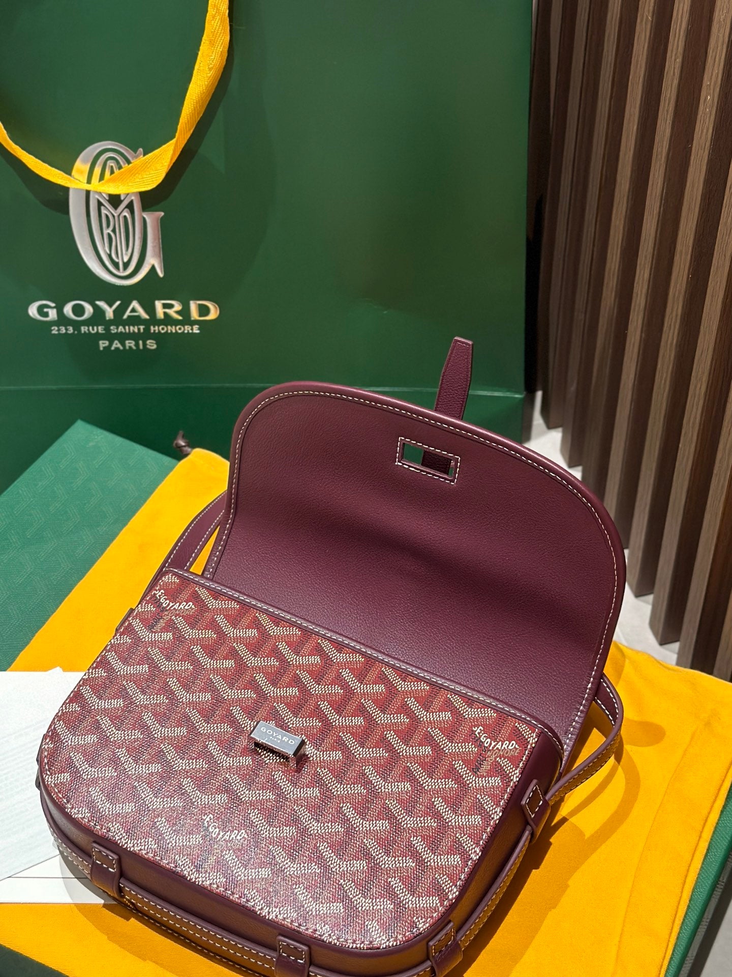 Goyard crossbody bag with patterned front, maroon leather top and clasp hardware