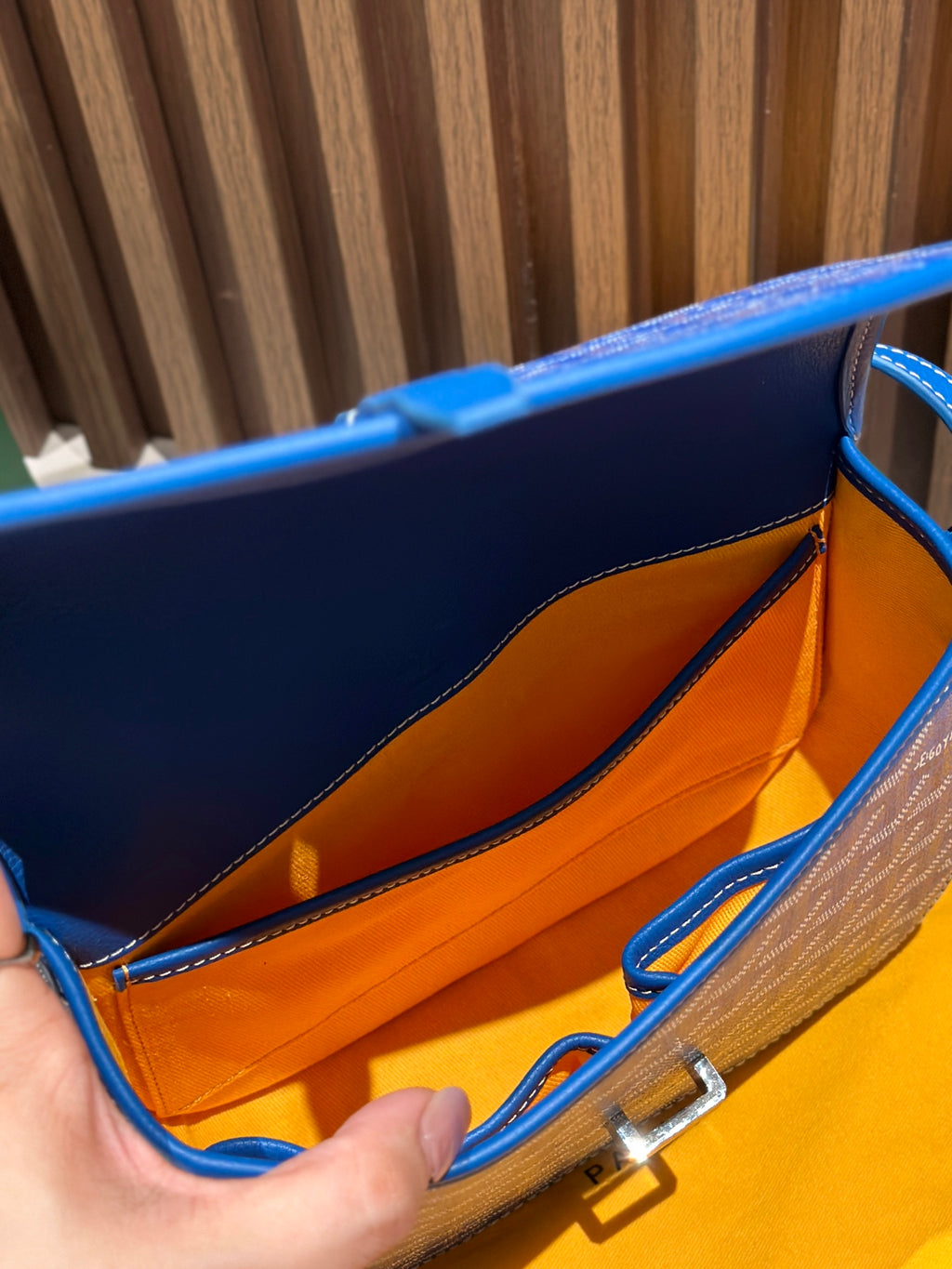 Goyard bag interior with orange lining and metal clasp, shown open by hands