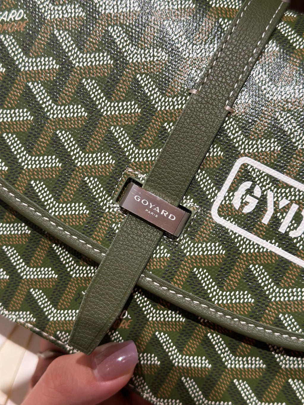 Green leather strap tab with Goyard Paris label and patterned canvas trim on crossbody bag.
