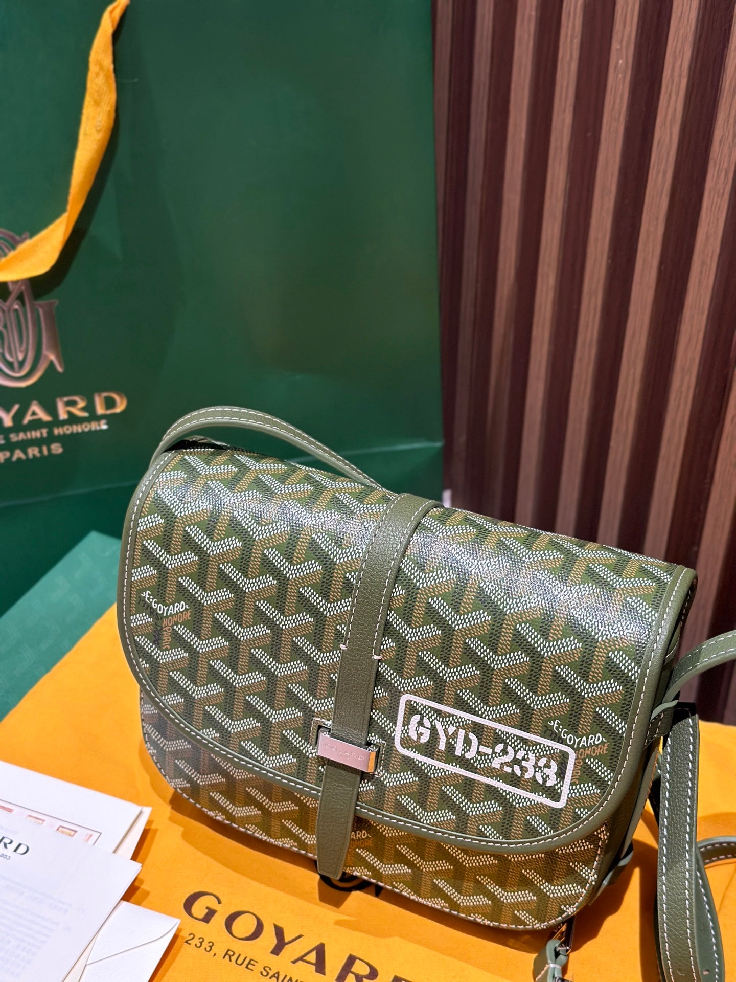 Small green crossbody bag with Goyardine pattern, front flap clasp, and side strap view.