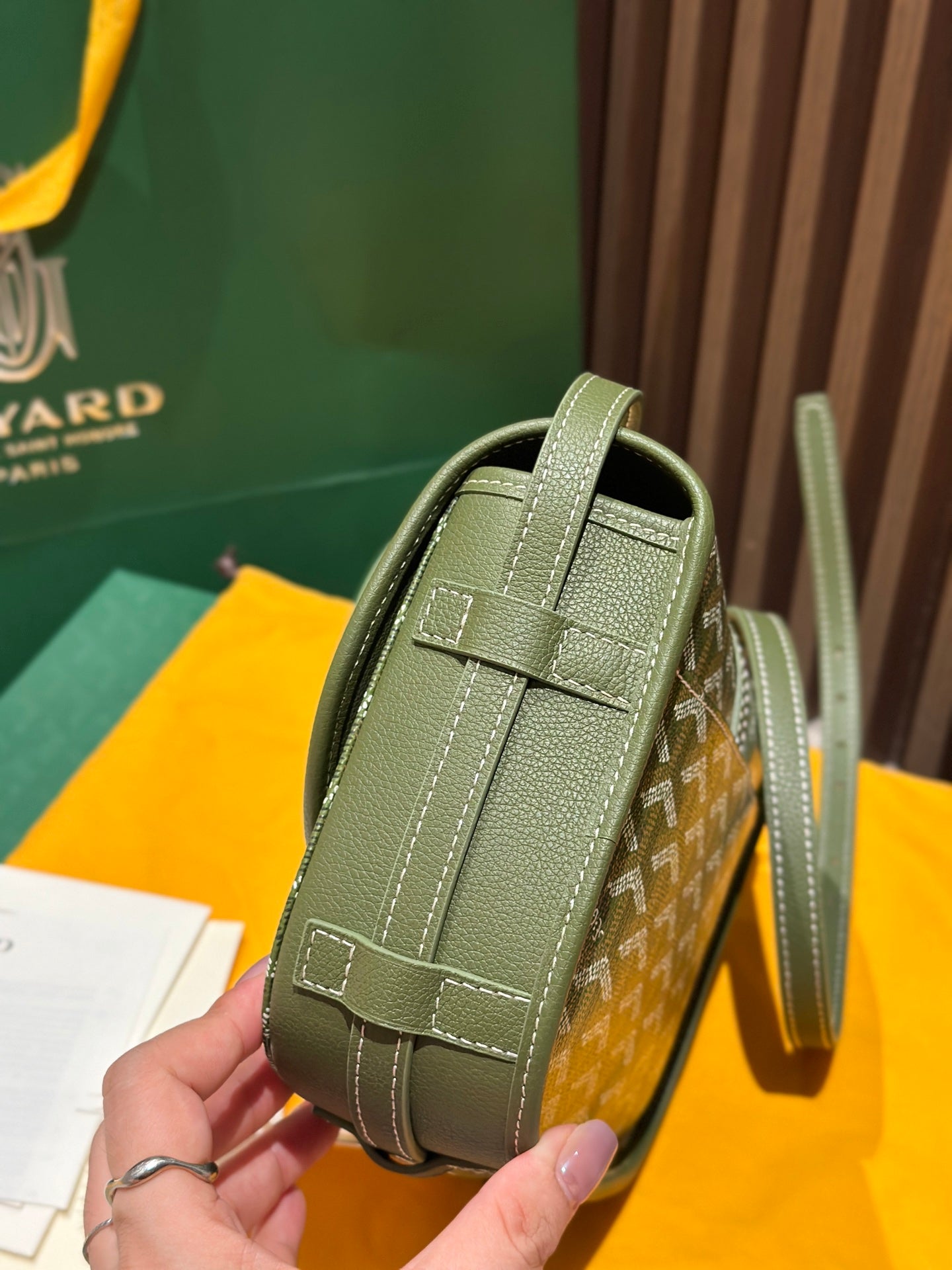 Green leather side panel of crossbody bag with stitched trim and strap hardware loop.