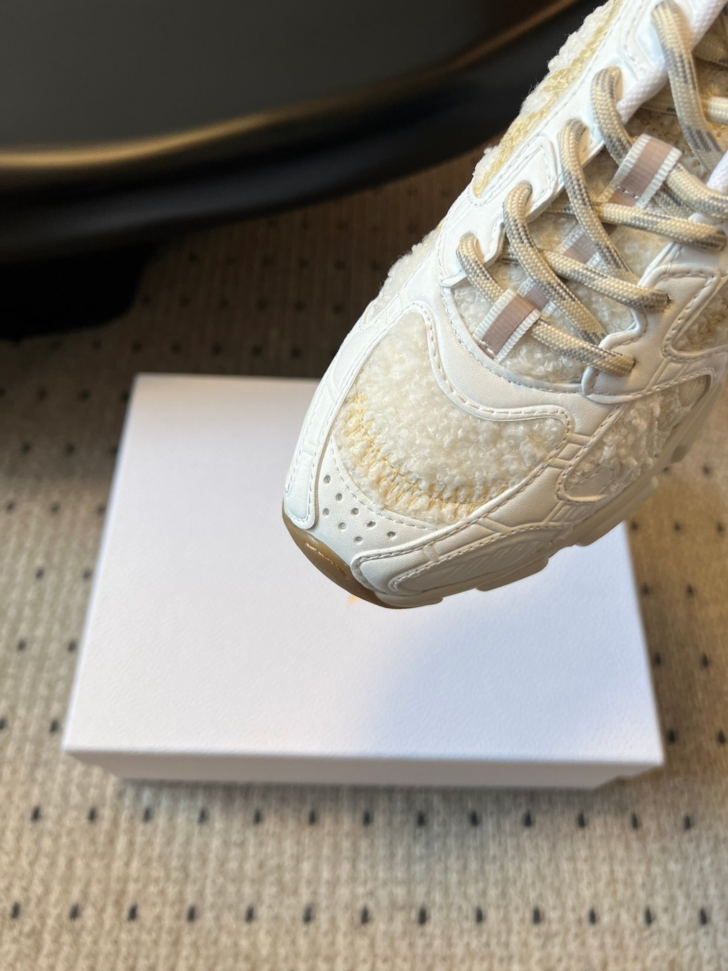 Dior unisex sneaker close-up, white leather with gold speckled logo and laces
