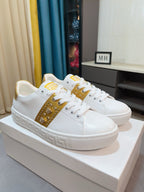 White and gold low-top sneakers with studded gold stripe and white lace-up