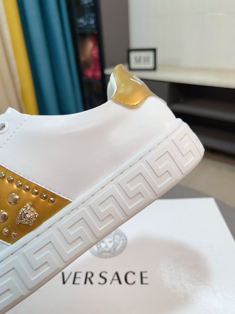 White low-top sneakers with gold studded stripe and Greek-key style sole