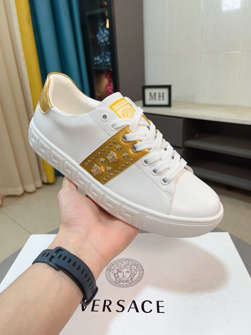 White low-top sneakers with gold side panel, studs, and gold logo patch