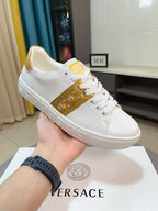 White low-top sneakers with gold side panel, studs, and gold logo patch
