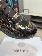 Black Versace sneakers with gold Greca pattern, lion charm, glossy toe cap and laces