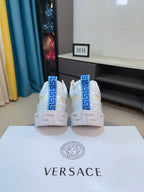 Pair of Versace white sneakers rear view with blue logo heel panels and molded soles.