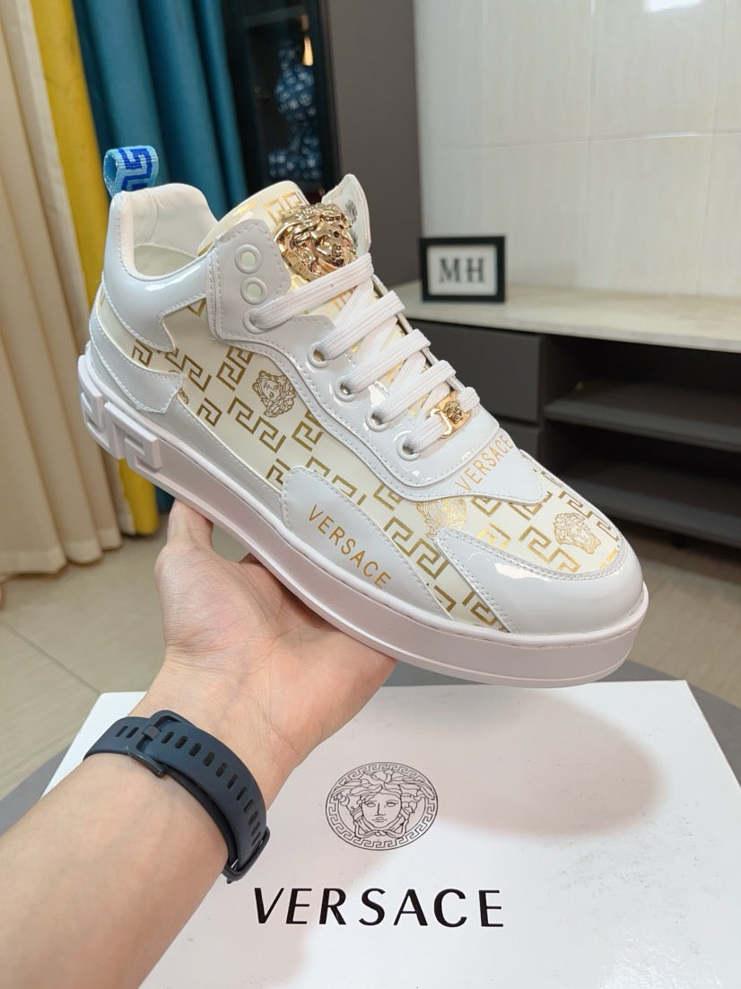 Versace white sneakers with gold lace overlay and Greek-key pattern detail, held up.