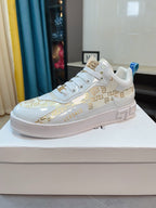 Versace white lace-up sneakers with gold patterned panel and blue heel pull tab.