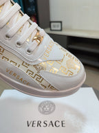 Versace white leather sneakers with gold and Greca logos, lace area close-up detail.
