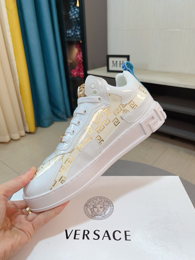 Versace white lace-up sneakers with gold logo print and chunky sole, held in hand.