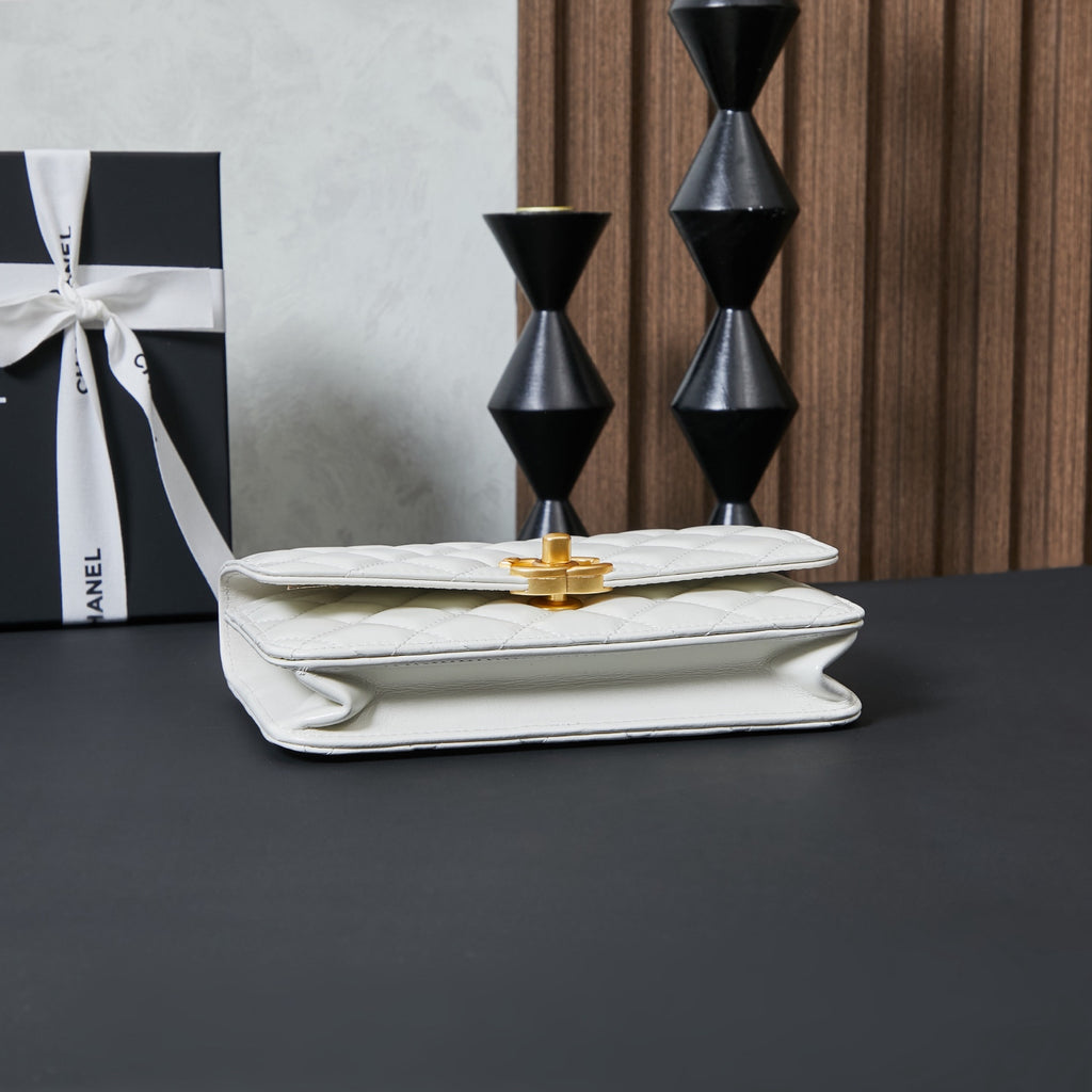 White Chanel bag with flap closed and gold-tone turn-lock clasp on front fold