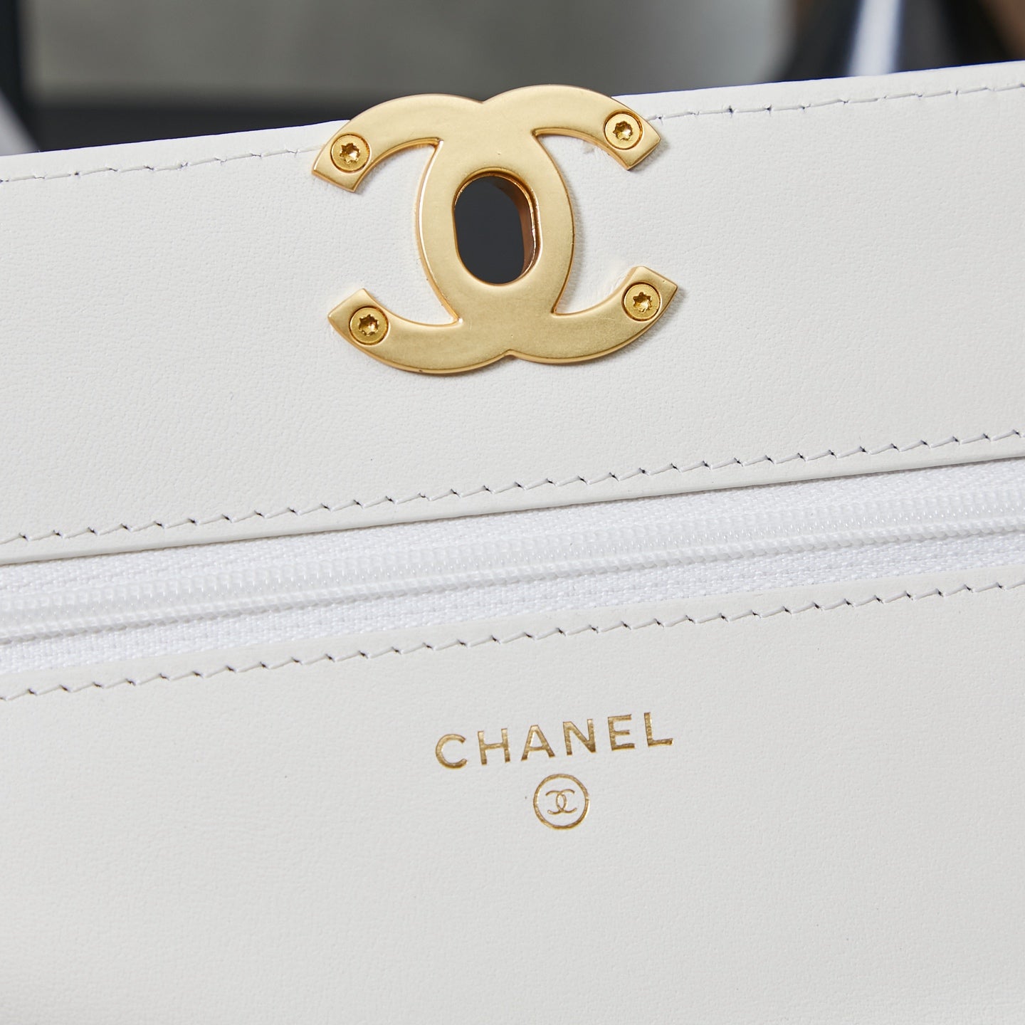 White Chanel bag close-up of gold CC logo emblem and small “CHANEL” stamp