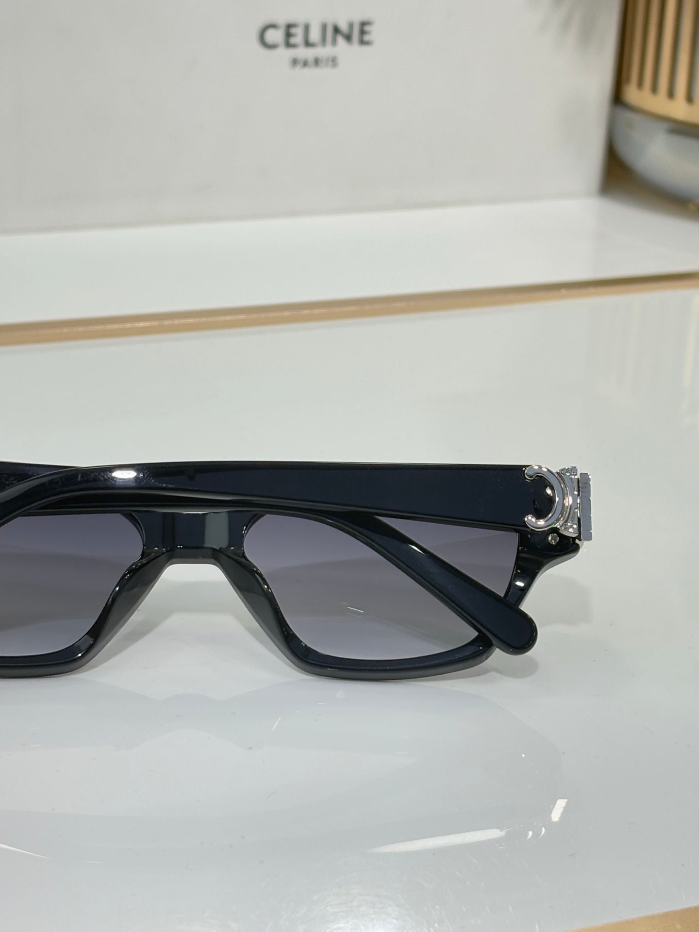 Side view of black cat-eye sunglasses with gold logo hinge and dark lenses