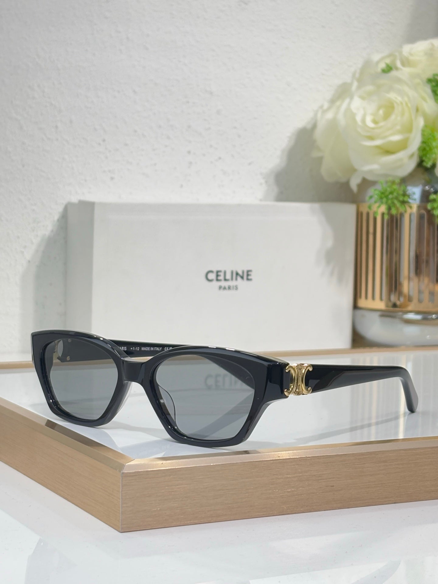 Black cat-eye sunglasses with gold logo detail and blue-tinted lenses on frame