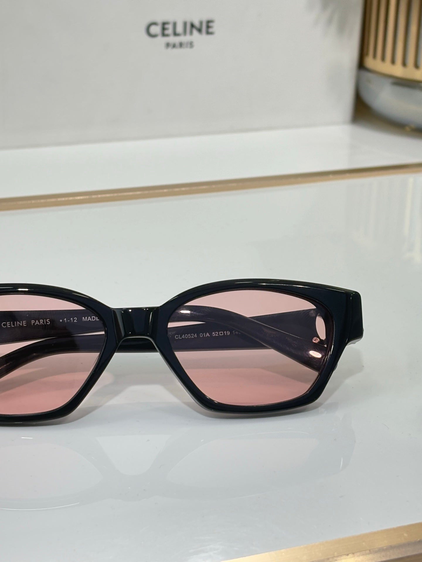 Close-up of black cat-eye sunglasses with gold logo and pink-tinted lenses