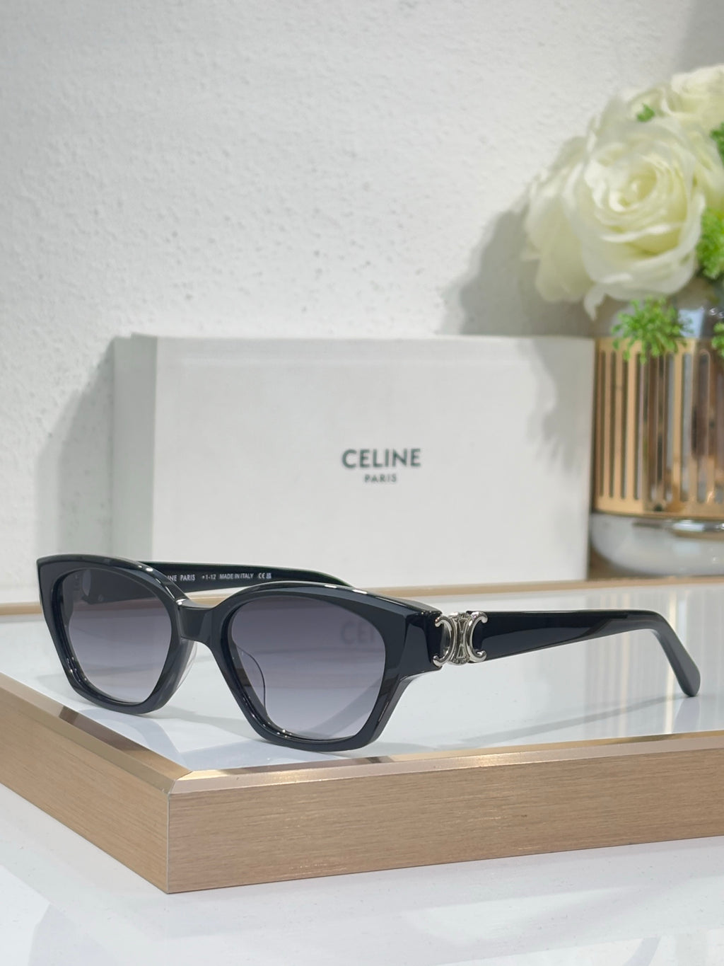 Black cat-eye sunglasses with gold logo detail and purple-tinted lenses on frame