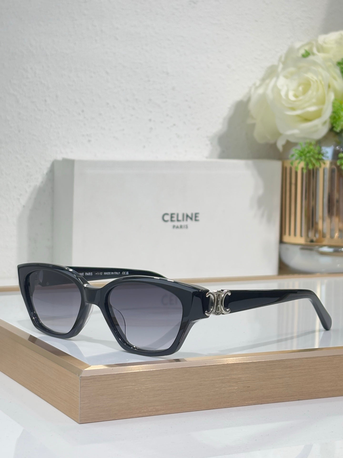 Black cat-eye sunglasses with gold logo detail and purple-tinted lenses on frame