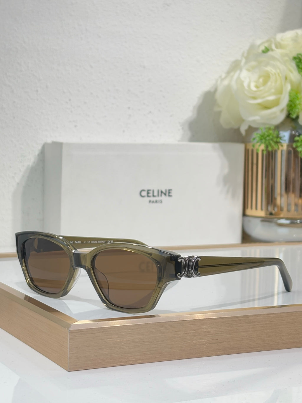 Black cat-eye sunglasses with gold logo detail and light brown-tinted lenses on frame