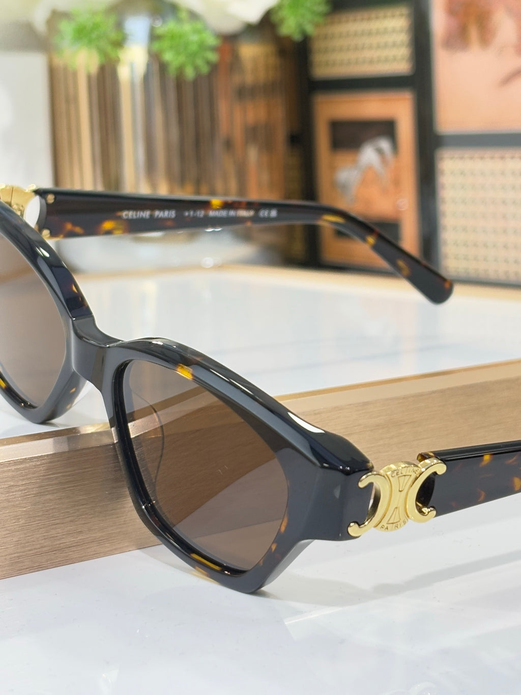 Angled view of black cat-eye sunglasses with gold logo detail and brown-tinted lenses