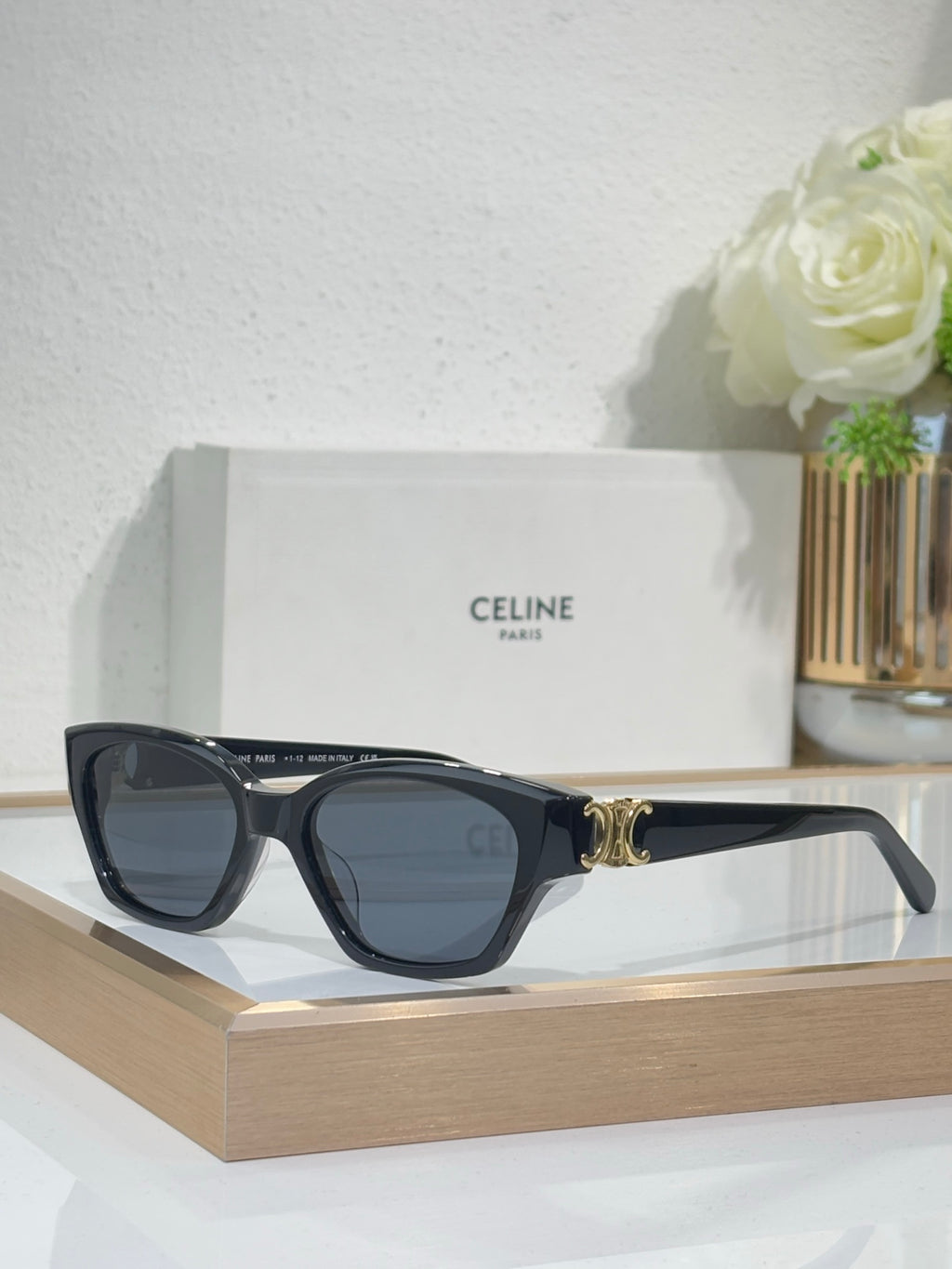 Black cat-eye sunglasses with gold logo detail and blue-tinted lenses on front view