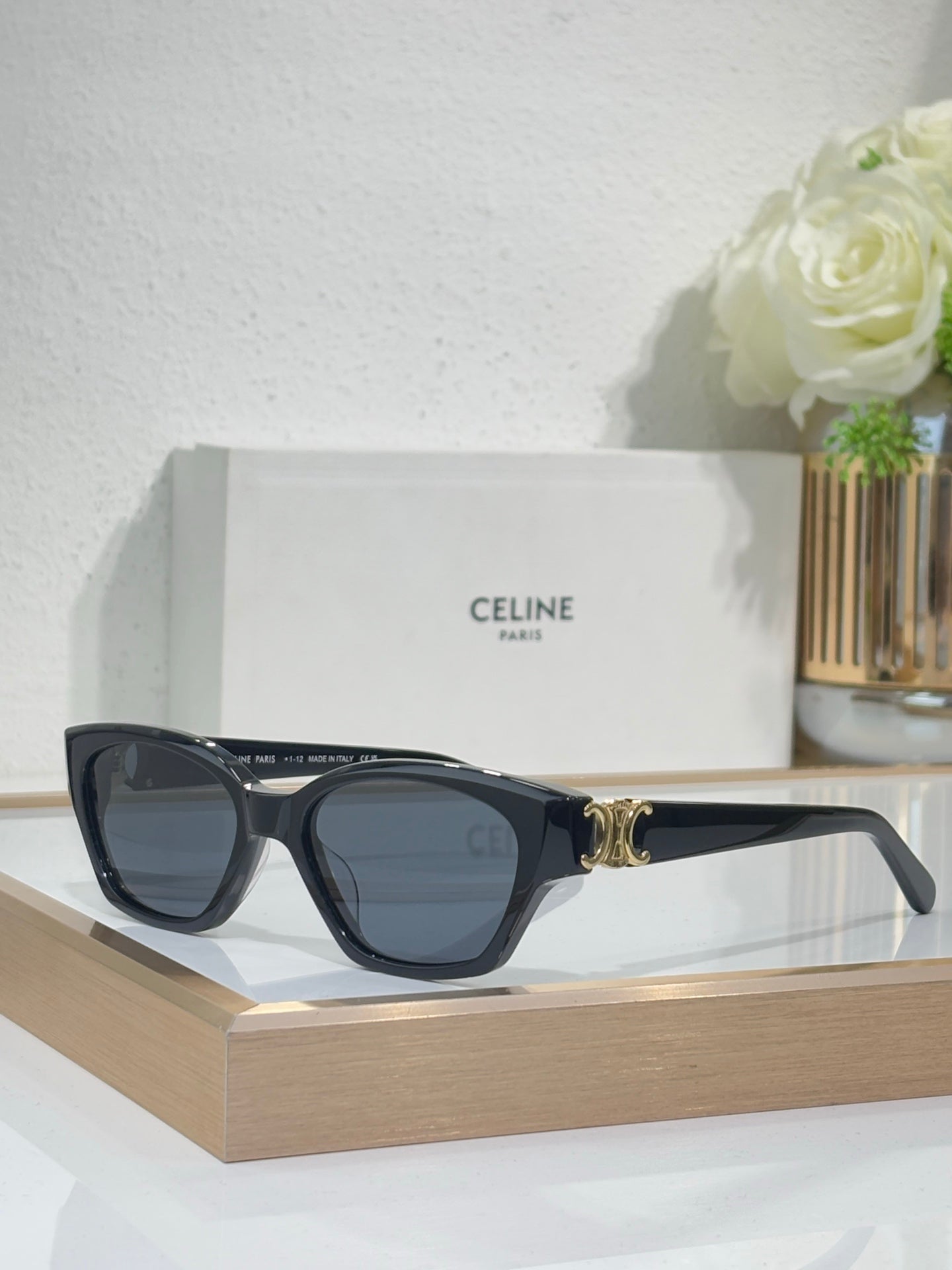 Black cat-eye sunglasses with gold logo detail and blue-tinted lenses on front view
