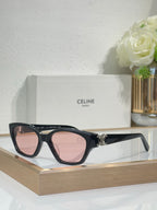 Black cat-eye sunglasses with gold logo detail and pink-tinted lenses on frame