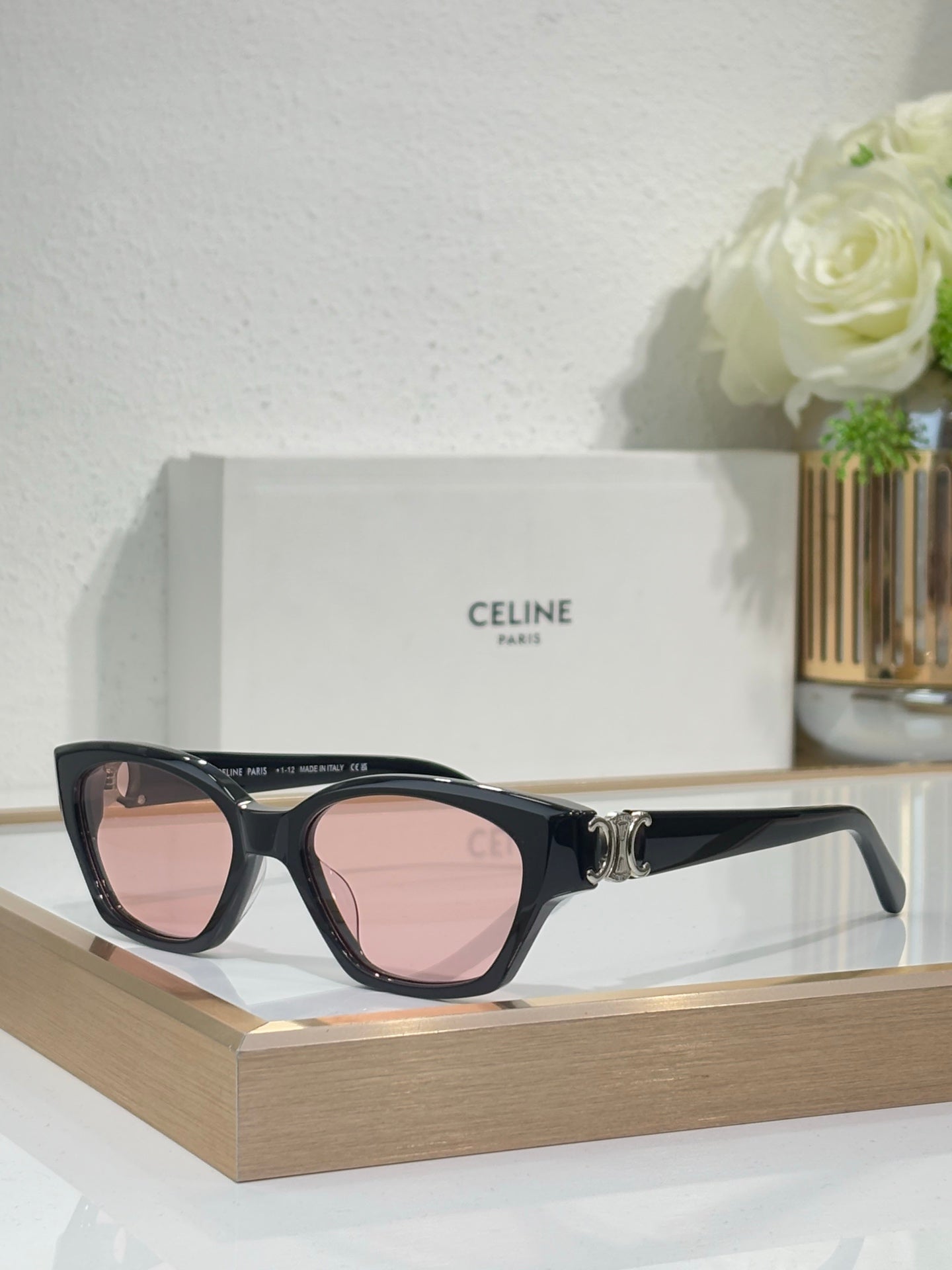 Black cat-eye sunglasses with gold logo detail and pink-tinted lenses on frame