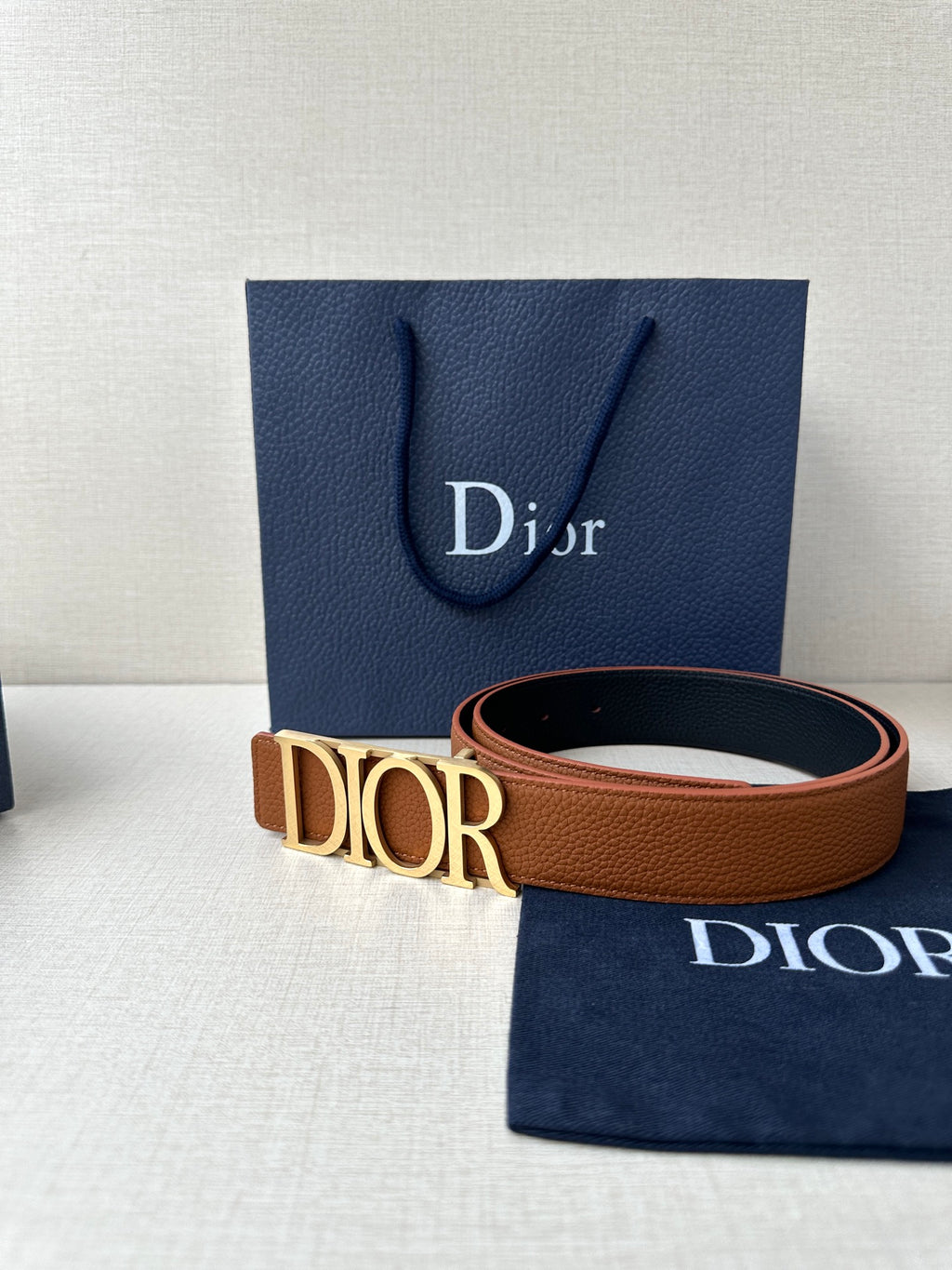 Tan leather Dior belt with engraved Dior buckle and visible strap edge.