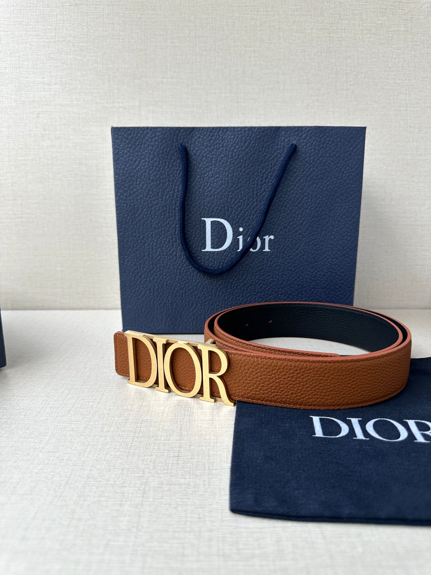 Tan leather Dior belt with engraved Dior buckle and visible strap edge.