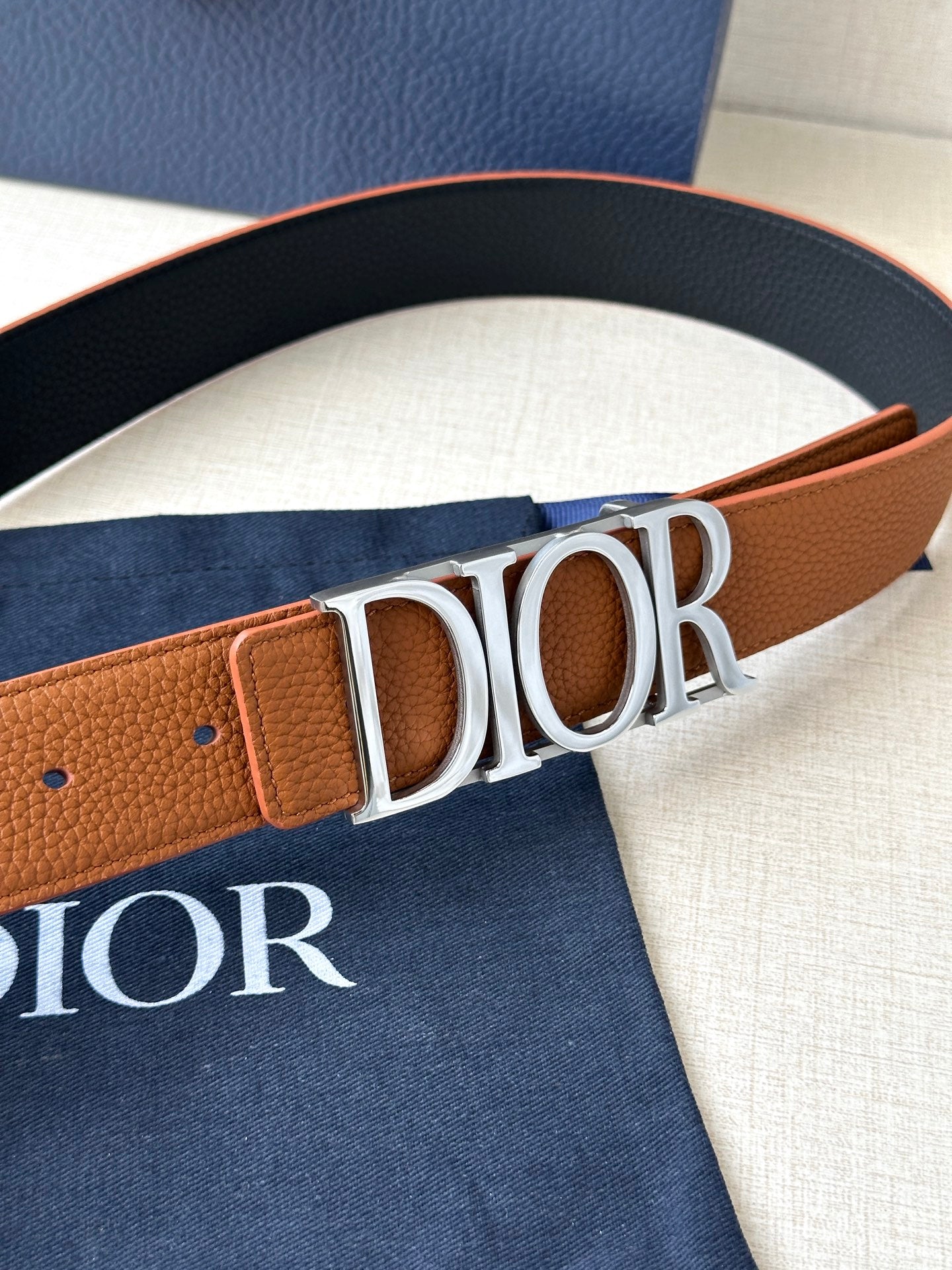 Tan and black Dior belt buckle detail with embossed letter logo on strap.