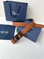 Tan leather Dior belt with engraved buckle, styled diagonally across packaging.