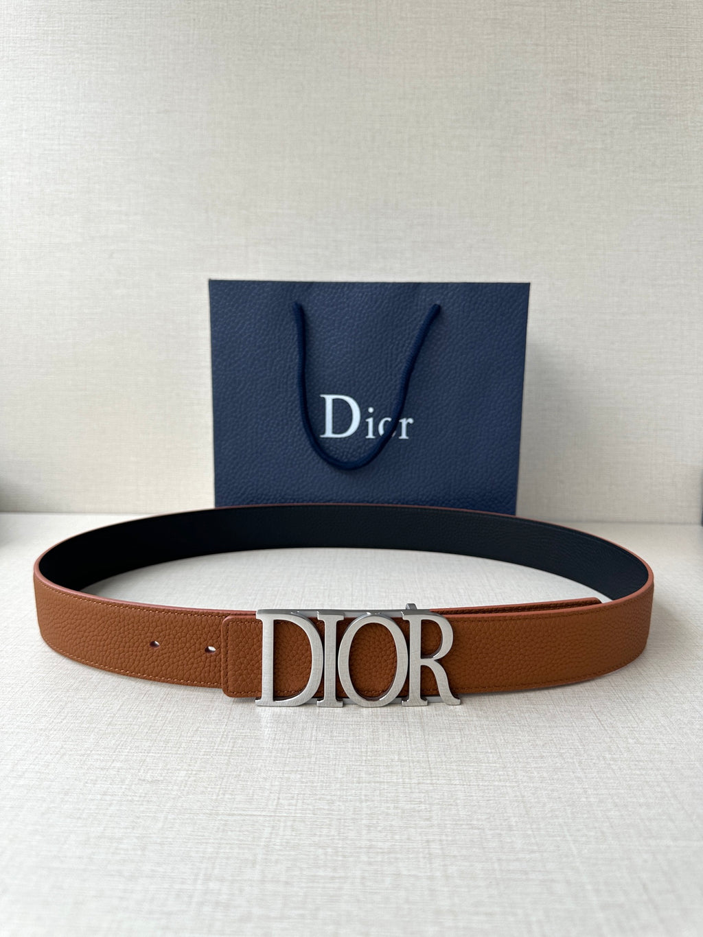 Tan leather Dior belt with rectangular engraved buckle on a flat strap.