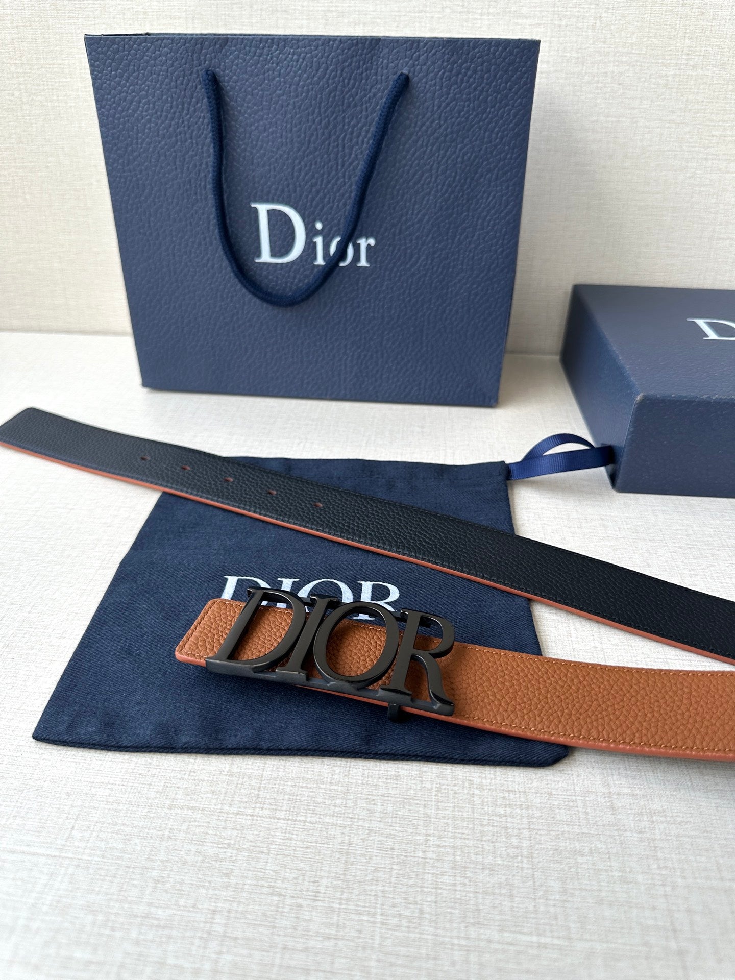 Tan leather Dior belt with dark buckle and strap, shown on blue cloth.