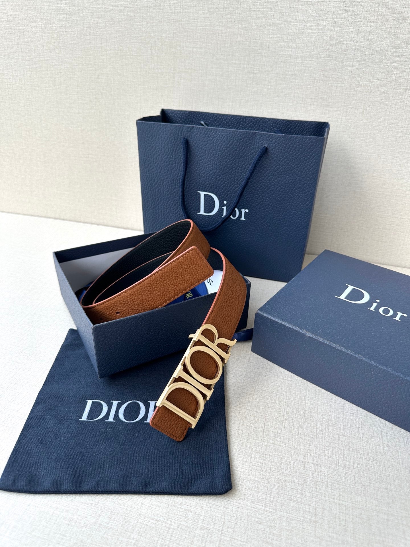 Tan Dior leather belt laid in gift set, buckle centered on the strap.