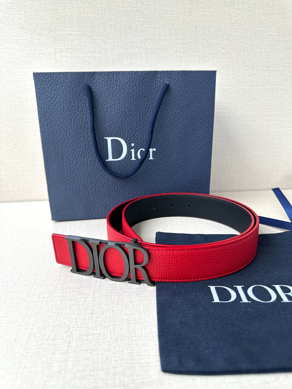 Dior red belt with gold “DIOR” buckle in front of packaging