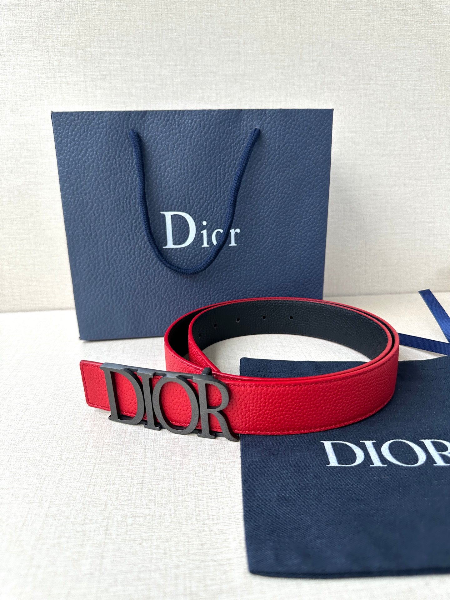 Dior red belt with gold “DIOR” buckle in front of packaging