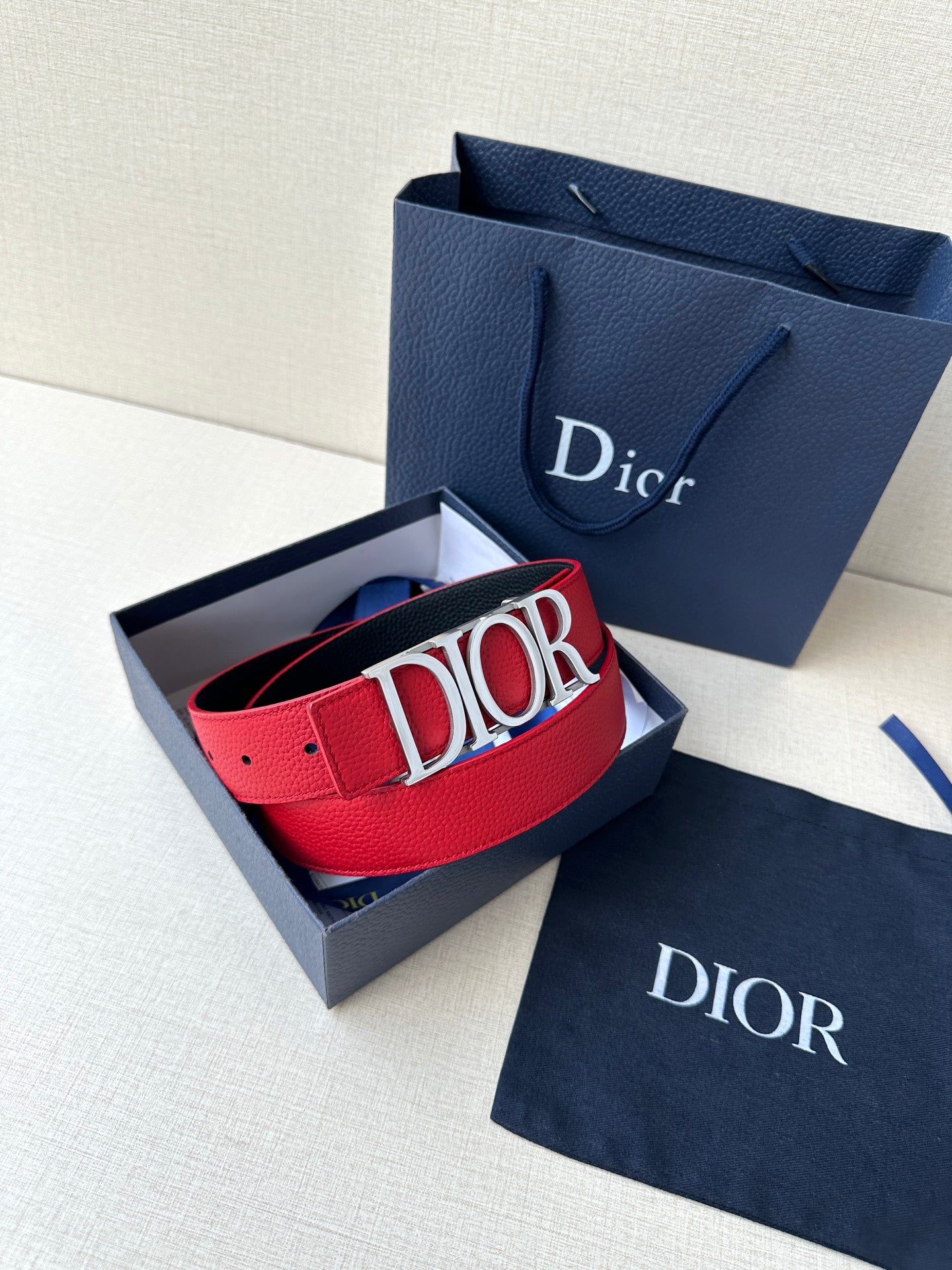 Dior red belt with gold “DIOR” buckle and blue branded bag