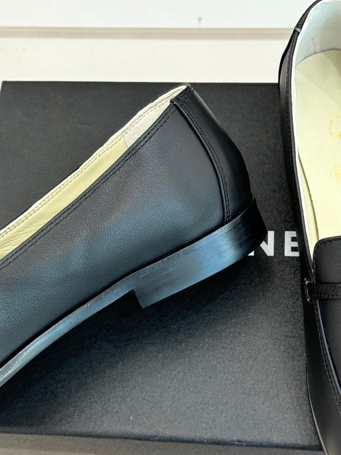 Close-up black leather loafer with gold-trimmed strap and low stacked heel
