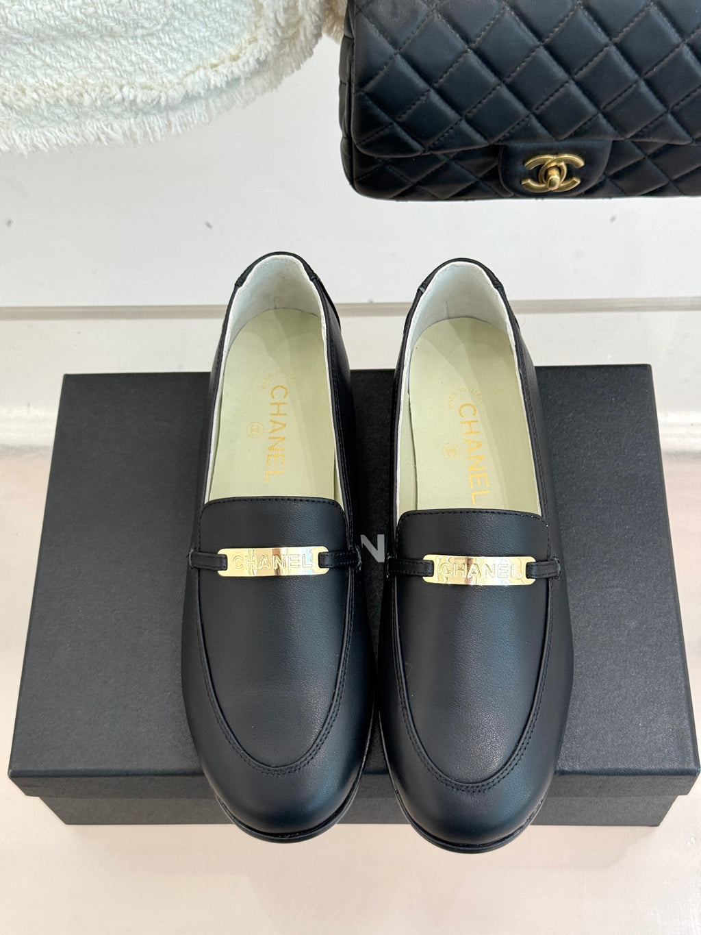 Black leather loafer pair with gold buckle bar and Chanel branding on box