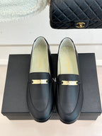 Black leather loafer pair with gold buckle bar and Chanel branding on box